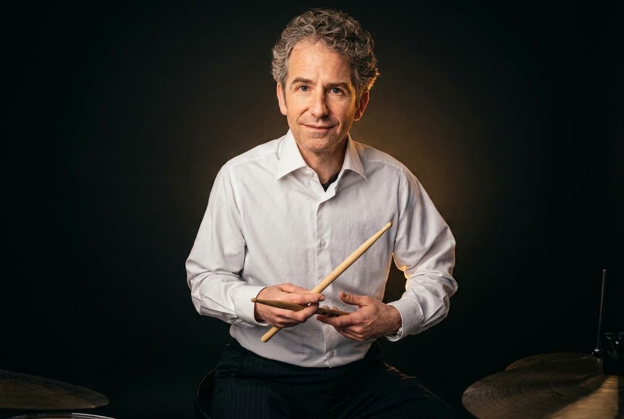Portrait von Benjamin Strauß mit Drumsticks im weissen Hemd vor dunklem Hintergrund